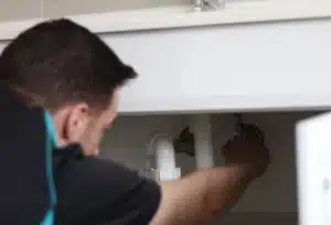 A hot water plumber turning on a hot water valve under a sink