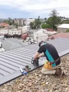A roof plumber drilling a gutter as part of their roof plumbing services